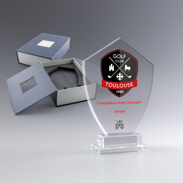 Trophée en verre transparent avec emblème du Golf Club Toulouse, présenté ouvert à côté de son écrin gris.